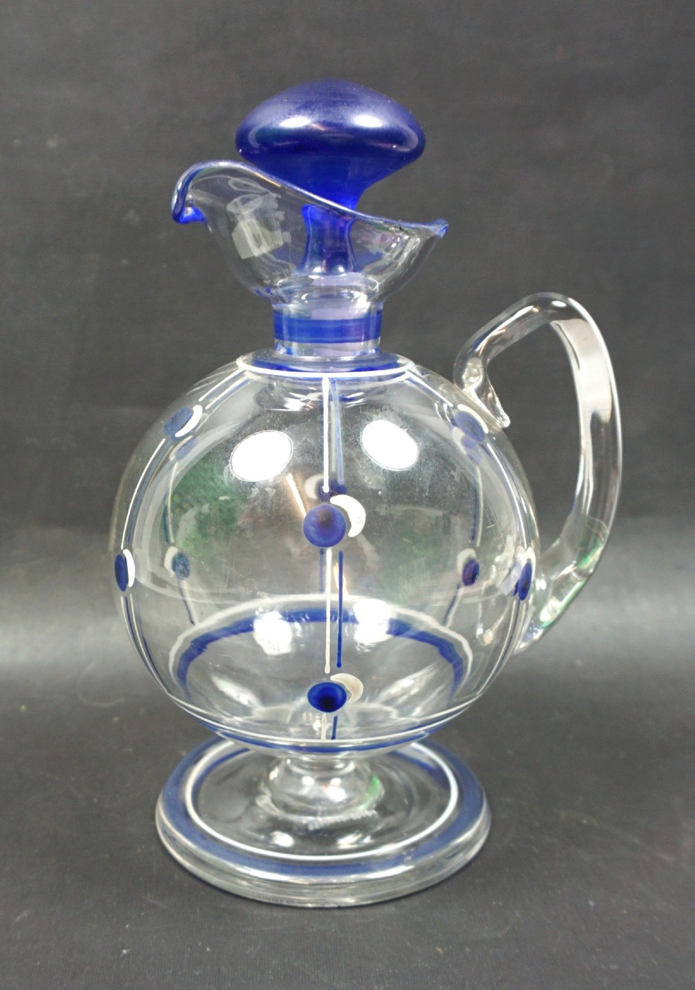 An Art Deco clear crystal glass wine jug featuring blue and white enamel geometric patterns, a clear handle, and a mushroom-shaped blue glass stopper.