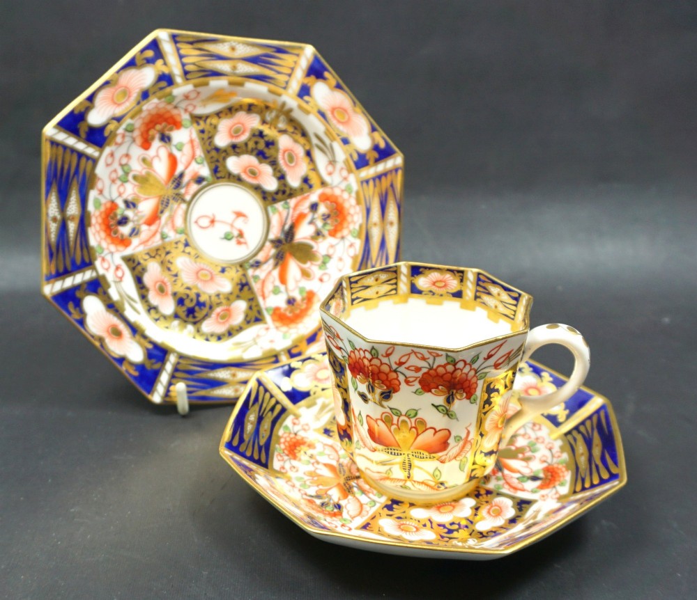 An octagonal Victorian Stevenson and Hancock Derby porcelain teacup, saucer, and side plate decorated in an Imari style pattern with cobalt blue, orange, and gold leaf gilding.