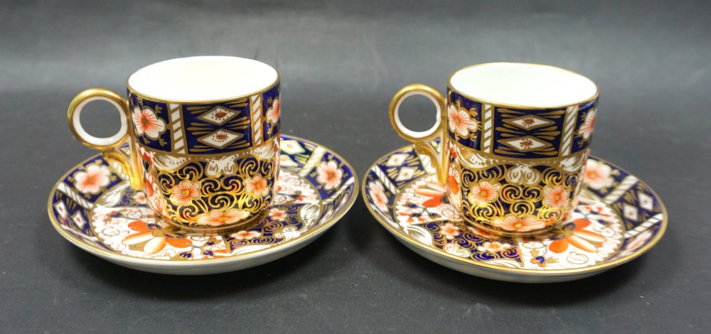 A pair of antique Royal Crown Derby porcelain coffee cans and matching saucers decorated in an Imari pattern with cobalt blue, iron red floral panels, and gold gilding.
