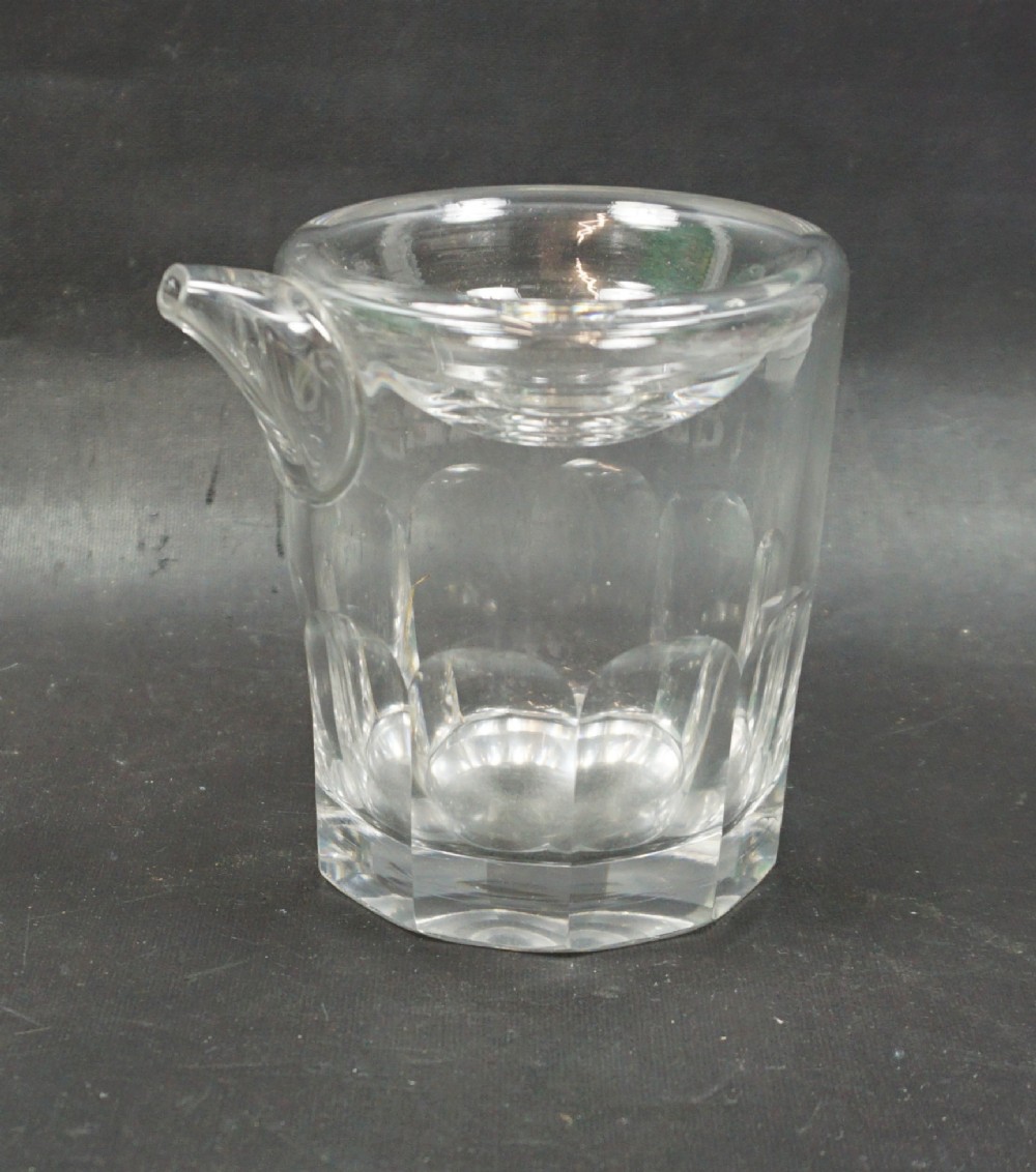 A clear heavy cut crystal glass feeding cup featuring an integrated spout and vertical flute cut detailing around the lower portion.