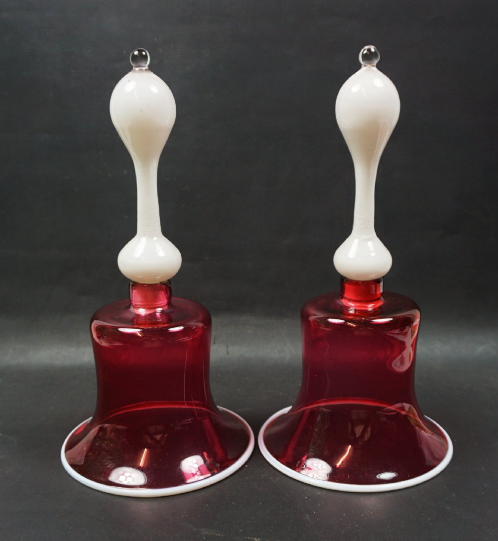 A pair of Victorian cranberry red glass bells featuring opaque white glass handles and matching white rim trims.