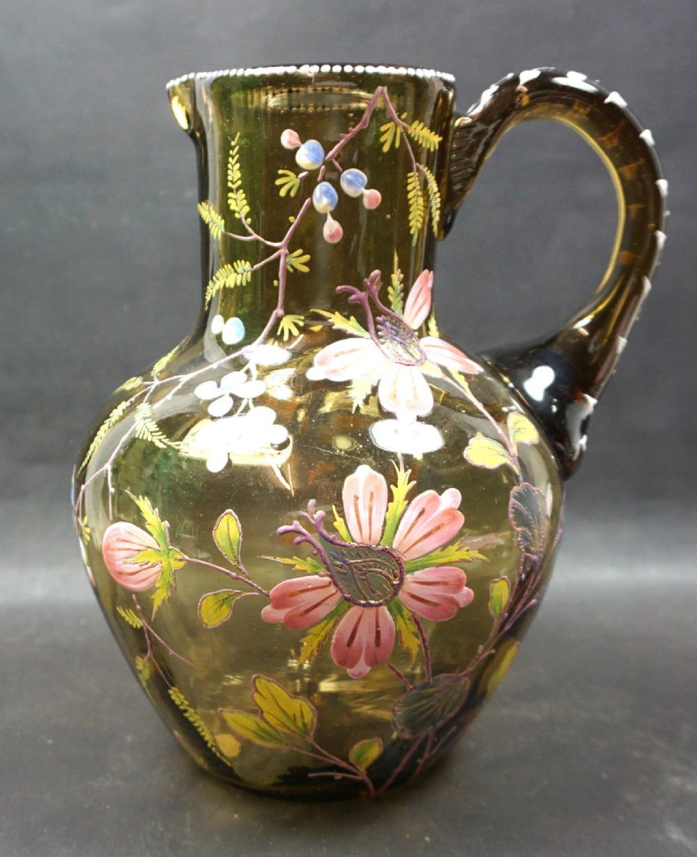 An olive green glass jug decorated with hand-painted enamelled pink flowers, green foliage, blue berries, and white beaded accents on the handle and rim.
