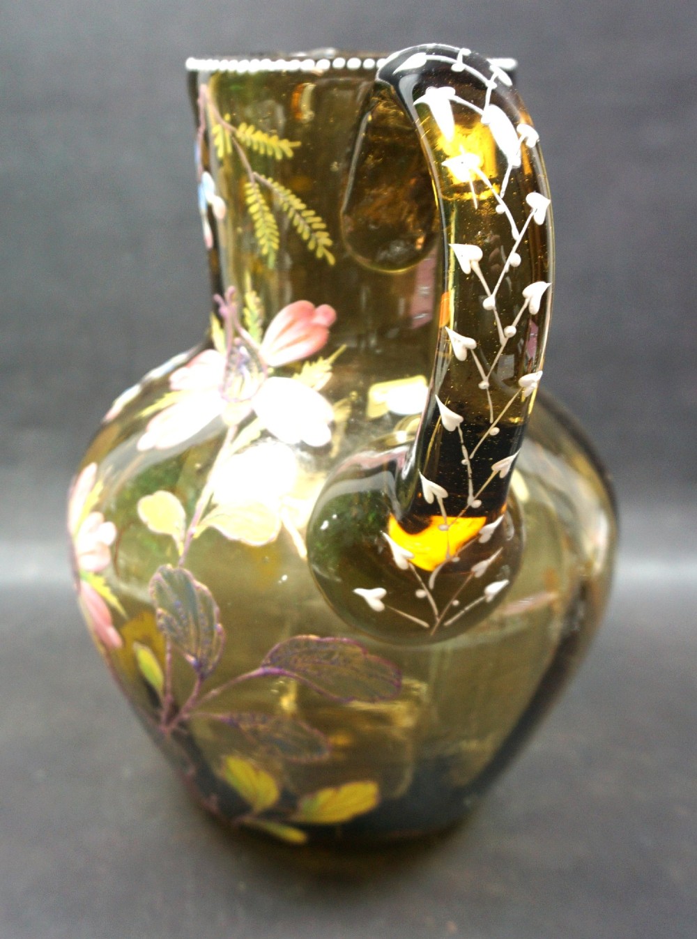 An olive green glass jug decorated with hand-painted enamelled pink flowers, green foliage, blue berries, and white beaded accents on the handle and rim. View II