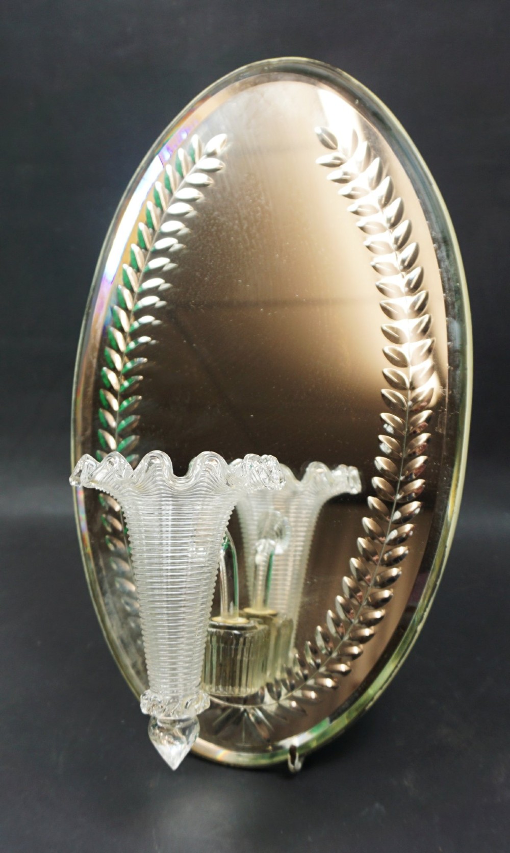 An oval silvered glass wall plaque featuring engraved leaf borders and a centrally mounted ribbed glass posey vase with a fluted rim. View II