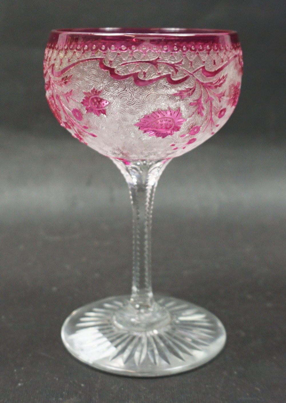 An acid-etched French lead crystal wine glass featuring a cranberry red foliate motif over a textured clear glass body on a slender stem with a starburst base.