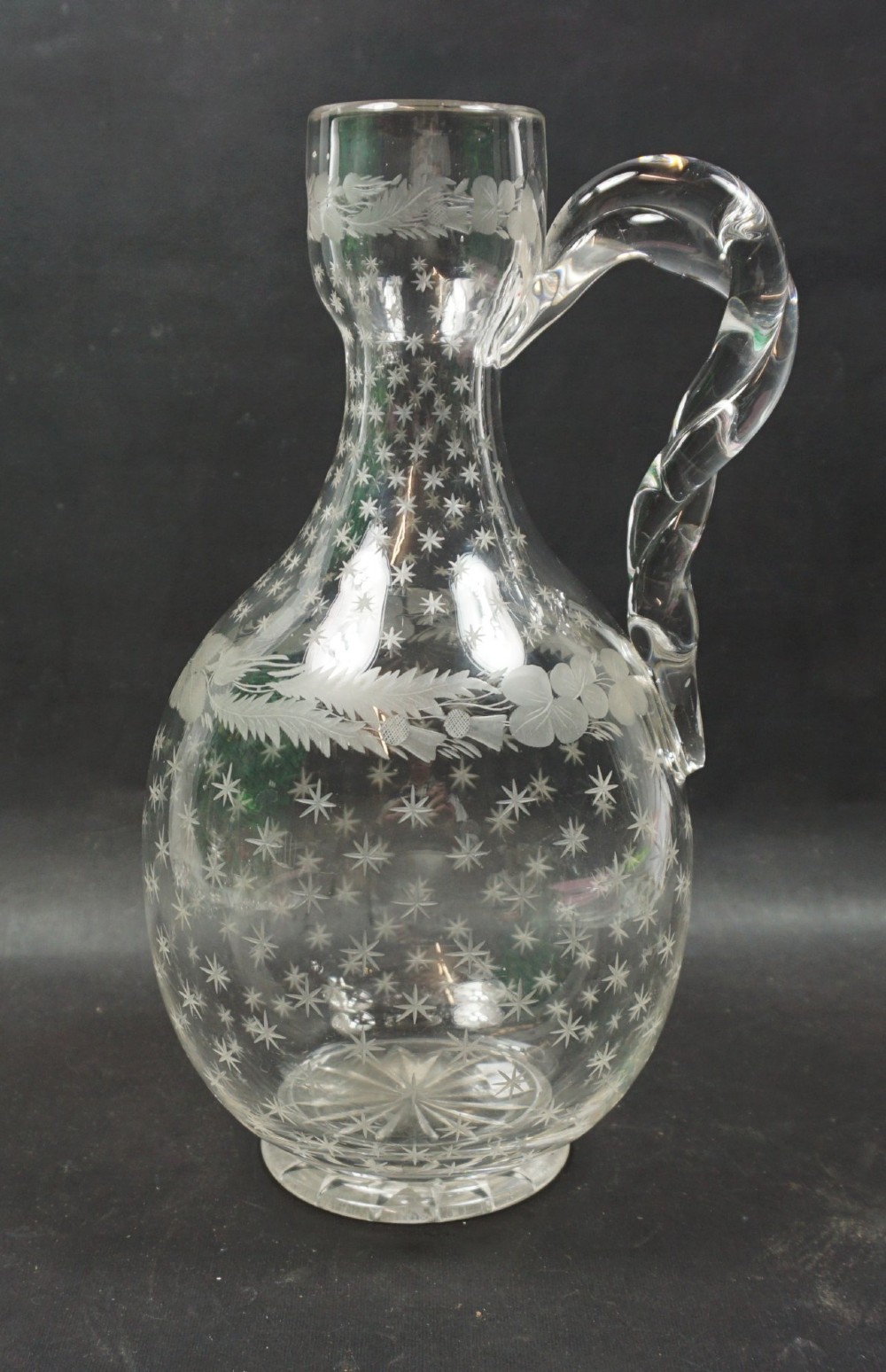 A clear Victorian crystal glass wine jug featuring engraved stars, Union floral motifs, and an applied twisted handle.