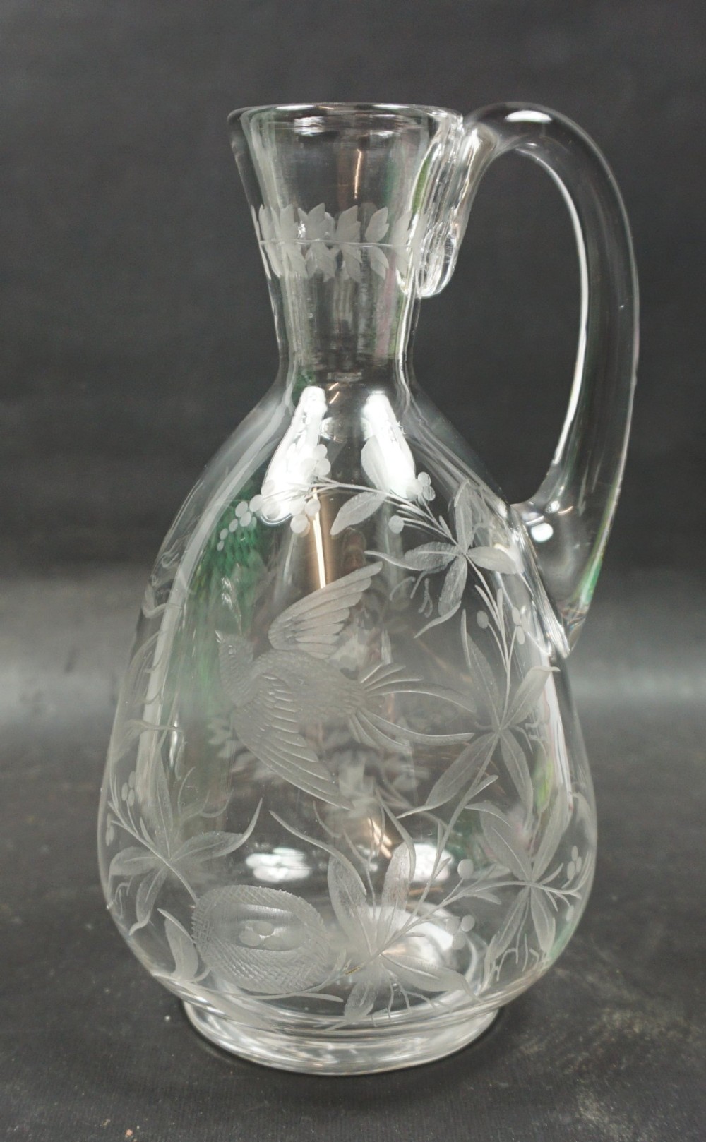 A clear glass jug featuring a single loop handle, flared rim, and detailed wheel-engraved motifs depicting a bird, nest with eggs, and foliage.