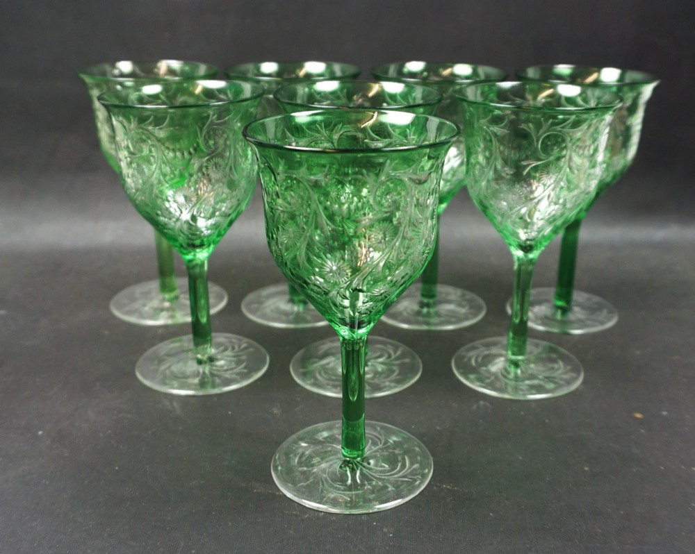 A set of eight green glass wine goblets featuring detailed intaglio engraved floral motifs and clear stemware bases.