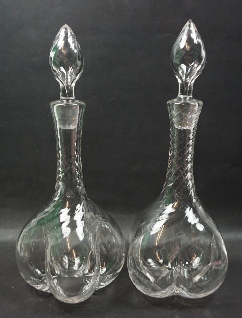 A pair of clear crystal glass decanters with spiralled ribbed necks, pinched lobed bases, and matching flame-shaped glass stoppers.