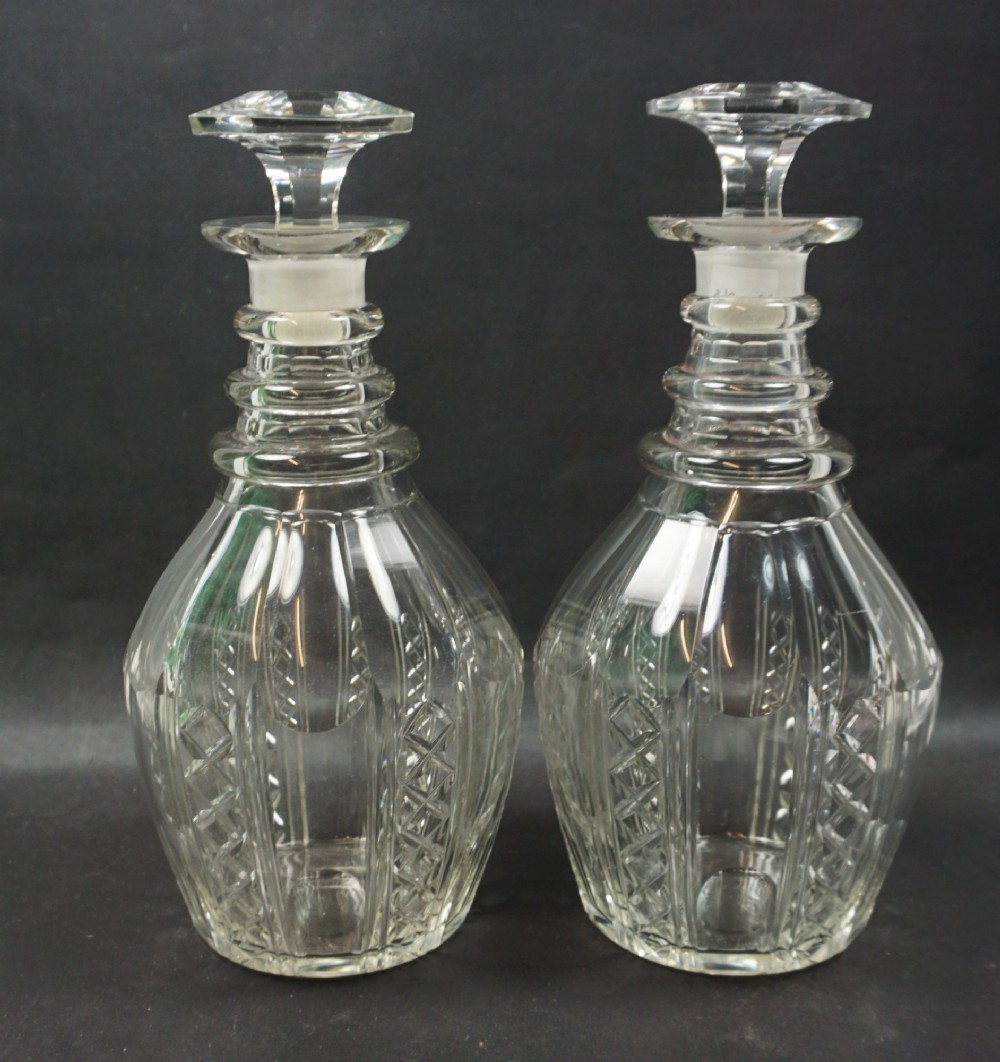 A pair of antique clear Regency cut glass decanters featuring ringed necks, geometric cut patterns, and mushroom stoppers.