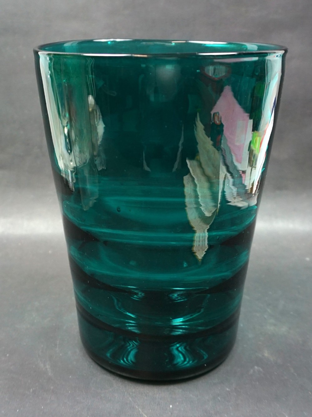 A cylindrical teal glass vase featuring horizontal ribbed banding along its tapered body.