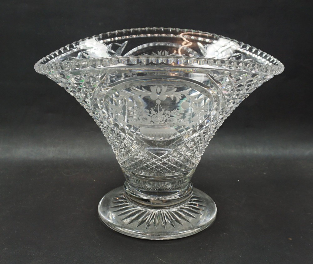 A clear cut lead crystal oval vase with wheel-engraved floral cartouches, diamond facet cutting, a scalloped rim, and a starburst circular foot.