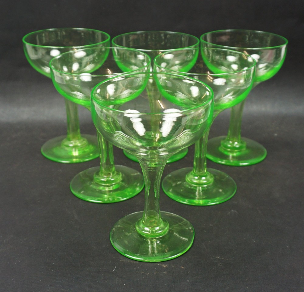 A set of six bright green uranium glass champagne coupes featuring hollow stems and circular bases.