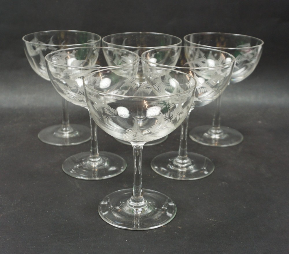 A set of six clear crystal champagne coupes with etched fern leaf motifs on shallow circular bowls and slender stems.
