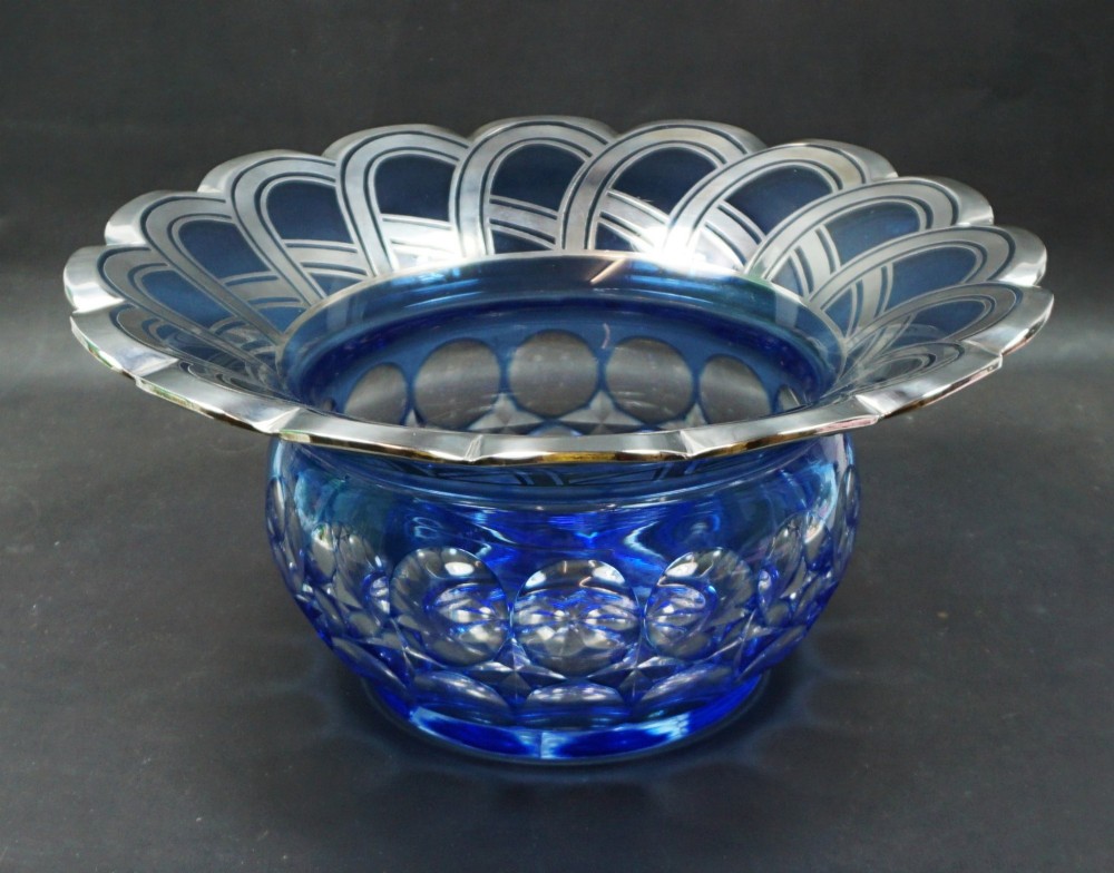 A cobalt blue cut crystal bowl featuring a flared scalloped rim decorated with geometric silver overlay arches and circular lens cuts around the lower body.
