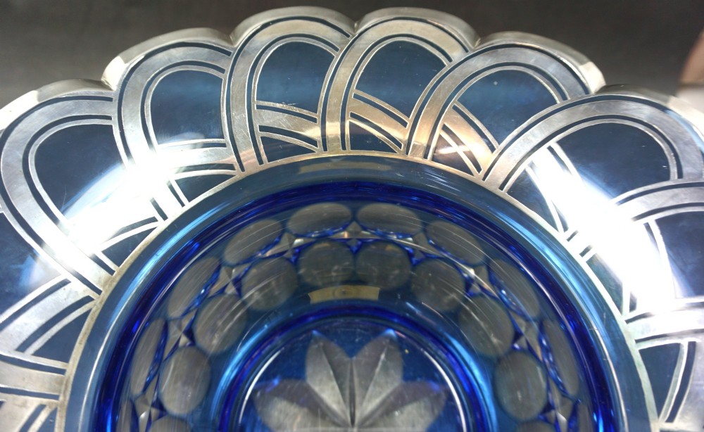 A cobalt blue cut crystal bowl featuring a flared scalloped rim decorated with geometric silver overlay arches and circular lens cuts around the lower body. View VI