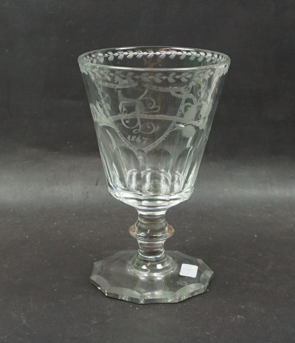 A clear glass marriage goblet featuring wheel-engraved foliage, a dated crest from 1847, a faceted lower bowl, and an octagonal cut foot.