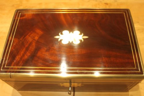 fig 1. A rectangular curl grain mahogany writing slope box featuring fine brass stringing, brass bound corners, a central brass cartouche, and a keyhole escutcheon.