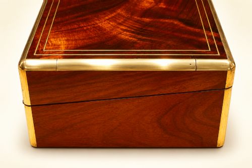 fig 1. An antique curl grain mahogany writing slope with fine brass stringing inlay, a decorative central brass cartouche, and a brass key inserted in the escutcheon.