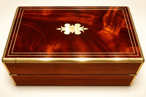 fig 2. An antique curl grain mahogany writing slope with fine brass stringing inlay, a decorative central brass cartouche, and a brass key inserted in the escutcheon.
