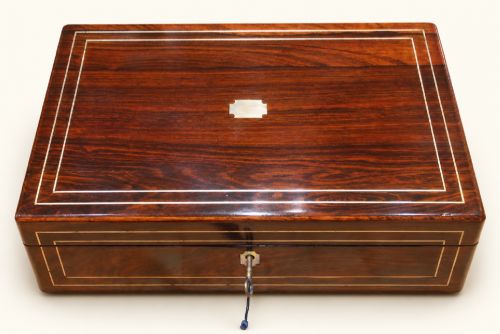 fig 1. A rectangular dark rosewood wooden writing slope featuring double brass stringing inlay, a central brass cartouche, and an escutcheon with an inserted key.