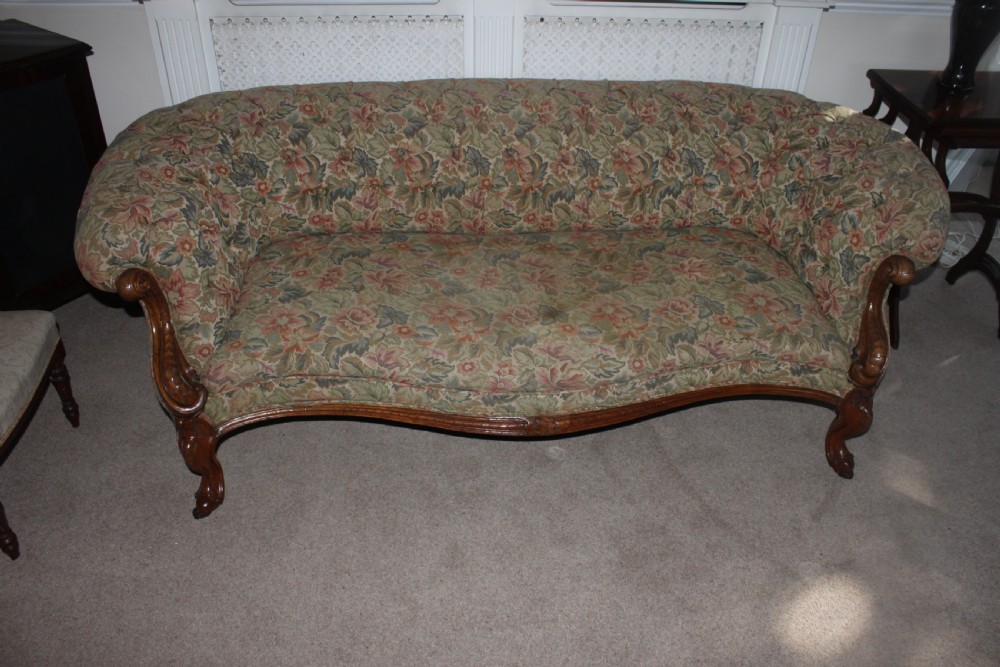 A Victorian carved walnut settee featuring button-tufted floral tapestry upholstery and scrolled wooden legs.