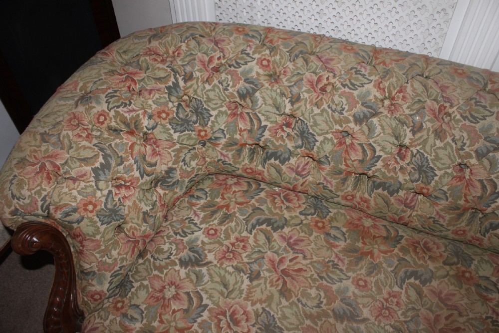 A Victorian carved walnut settee featuring button-tufted floral tapestry upholstery and scrolled wooden legs. View XV