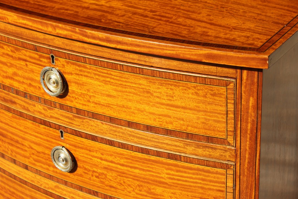 A tall Sheraton Revival satinwood bow front chest featuring six drawers with inlaid crossbanded borders, central brass ring handles, and splayed bracket feet. View III