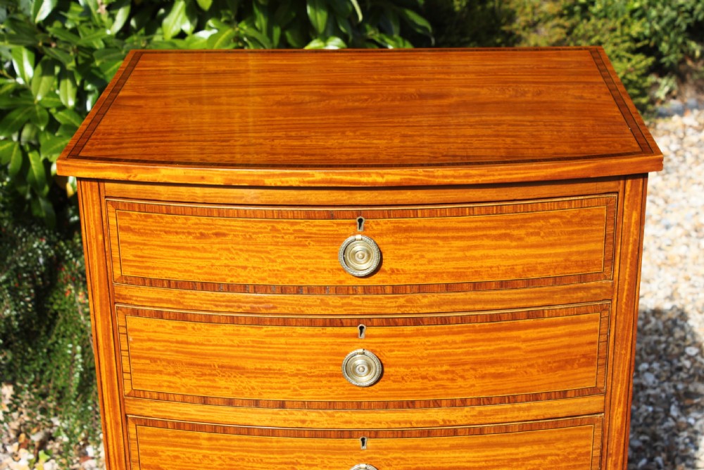 A tall Sheraton Revival satinwood bow front chest featuring six drawers with inlaid crossbanded borders, central brass ring handles, and splayed bracket feet. View VII