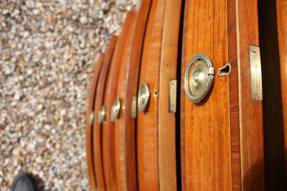 A tall Sheraton Revival satinwood bow front chest featuring six drawers with inlaid crossbanded borders, central brass ring handles, and splayed bracket feet. View IX