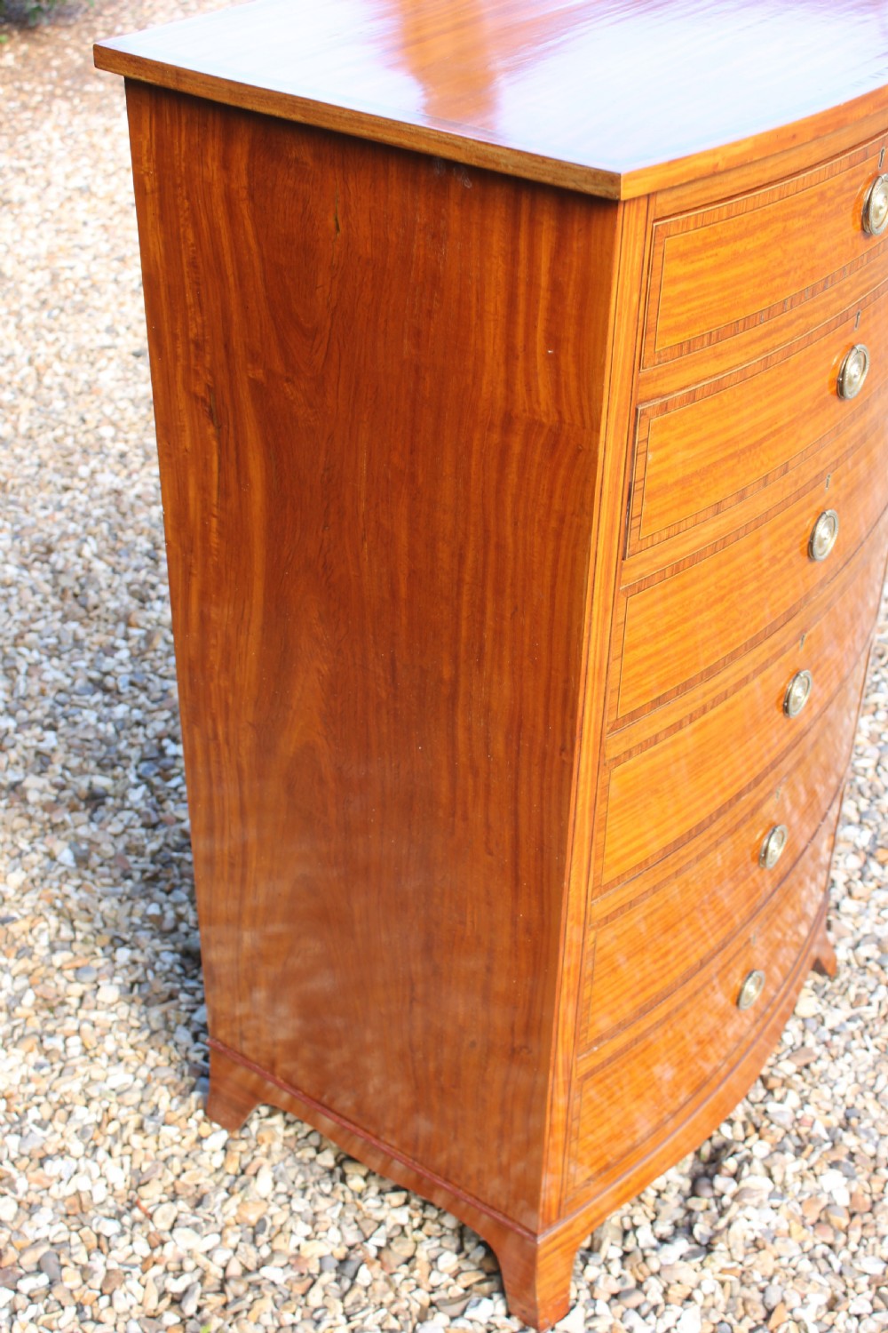 A tall Sheraton Revival satinwood bow front chest featuring six drawers with inlaid crossbanded borders, central brass ring handles, and splayed bracket feet. View XII