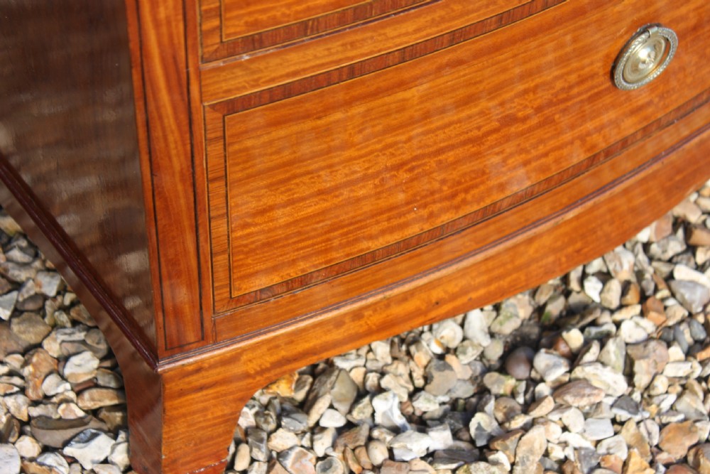 A tall Sheraton Revival satinwood bow front chest featuring six drawers with inlaid crossbanded borders, central brass ring handles, and splayed bracket feet. View XIII
