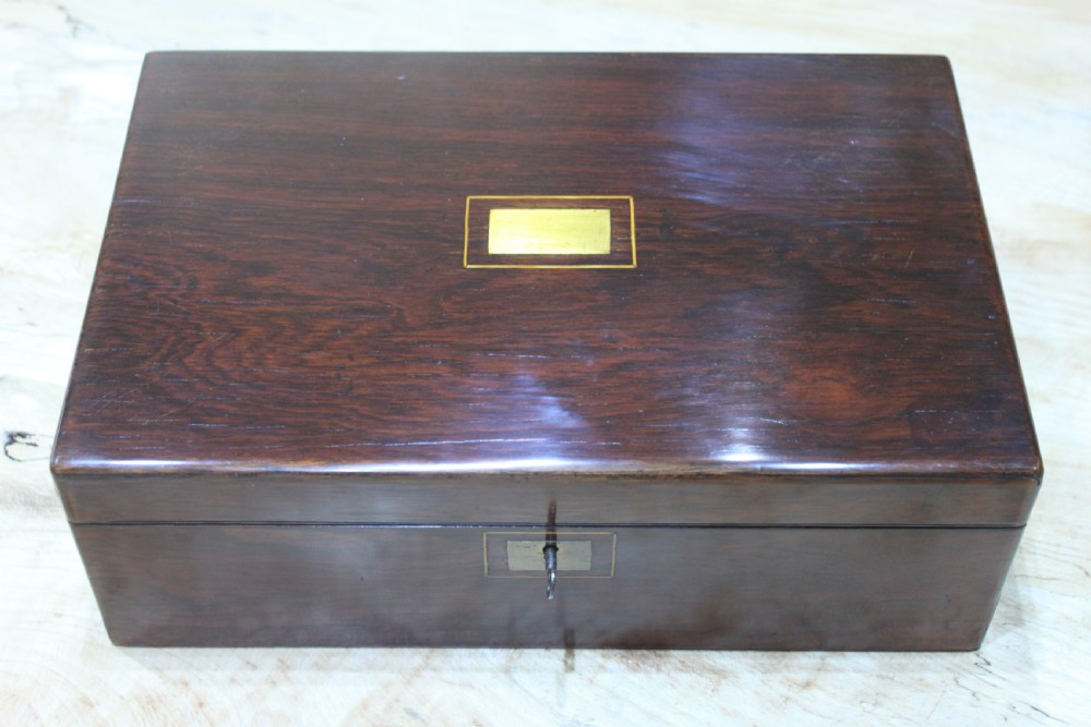 A rectangular dark rosewood writing slope box featuring a central brass cartouche and key inserted in the front lock.