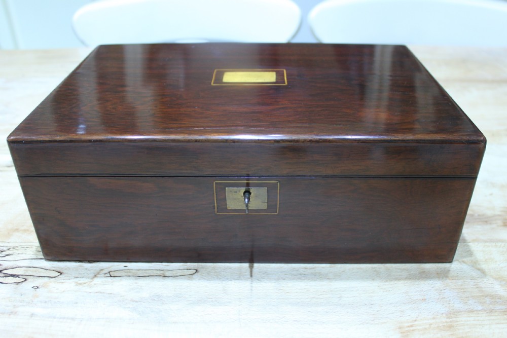 A rectangular dark rosewood writing slope box featuring a central brass cartouche and key inserted in the front lock. View VII