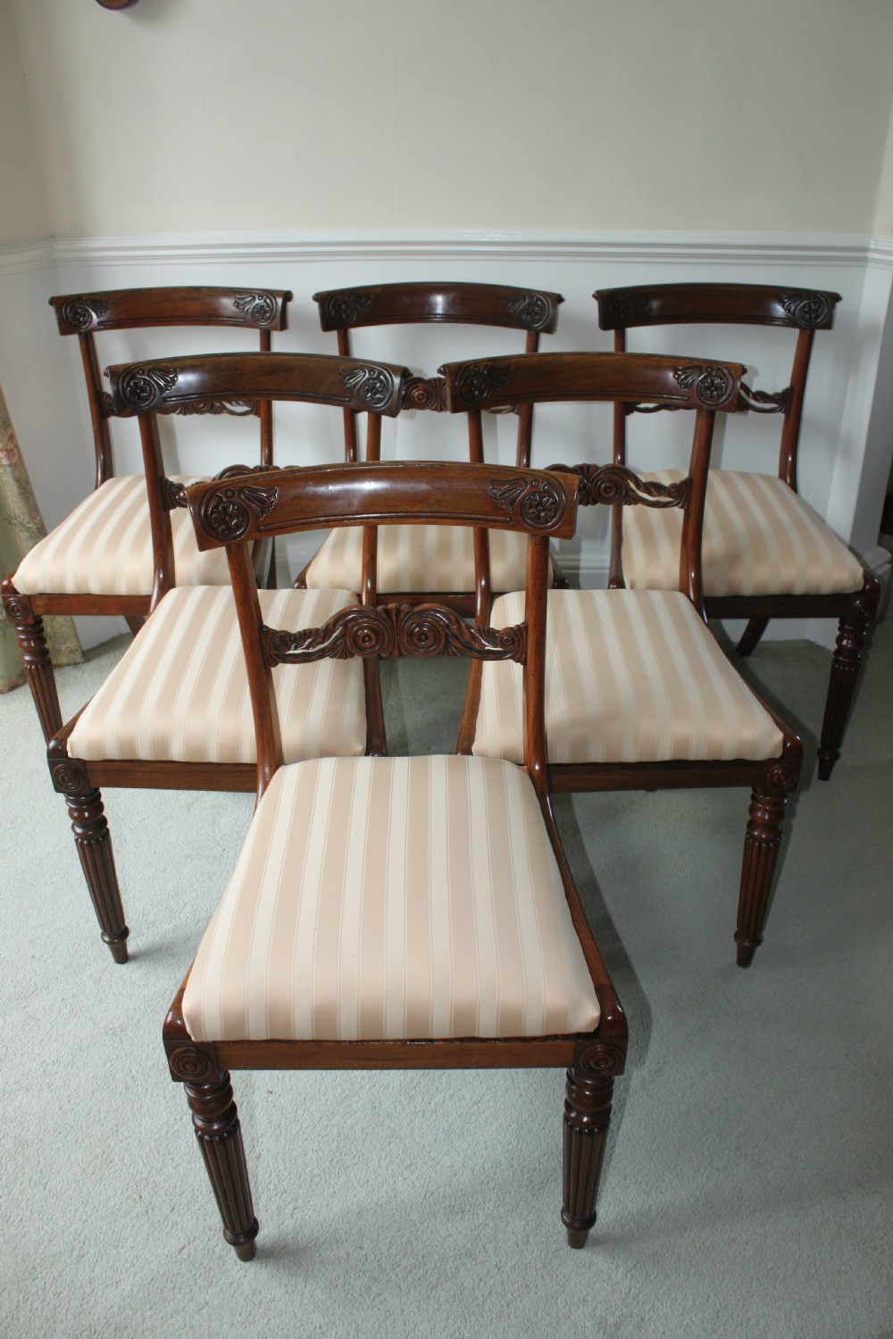 A set of six dark mahogany Regency dining chairs featuring carved top rails, reeded front legs, and cream striped fabric seats.