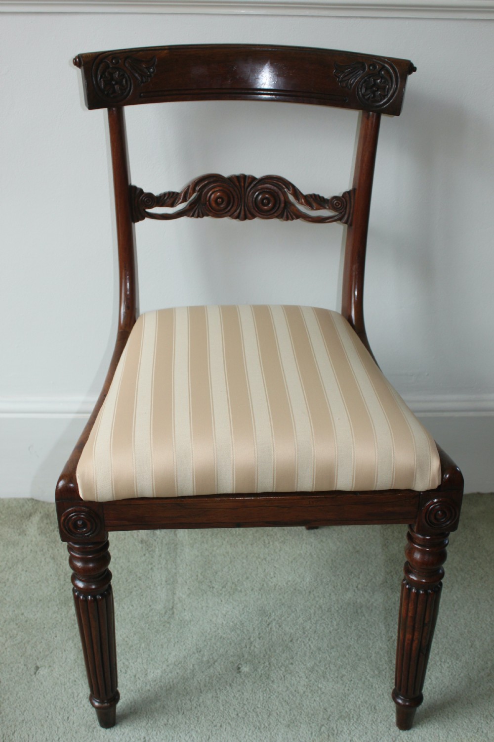 A set of six dark mahogany Regency dining chairs featuring carved top rails, reeded front legs, and cream striped fabric seats. View II