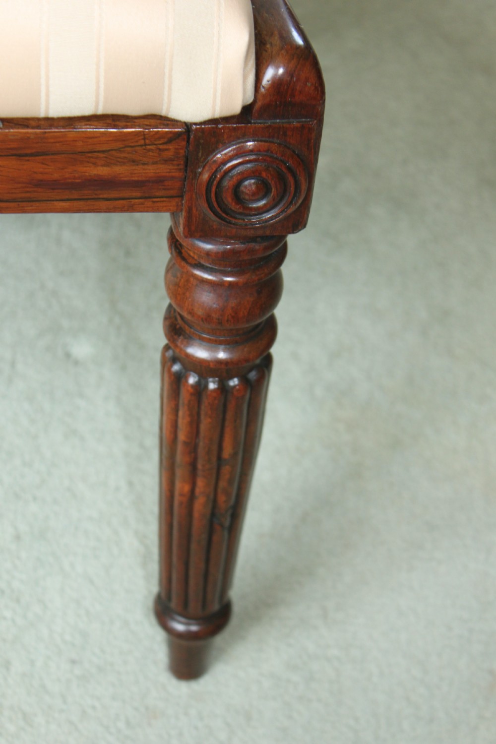 A set of six dark mahogany Regency dining chairs featuring carved top rails, reeded front legs, and cream striped fabric seats. View VII