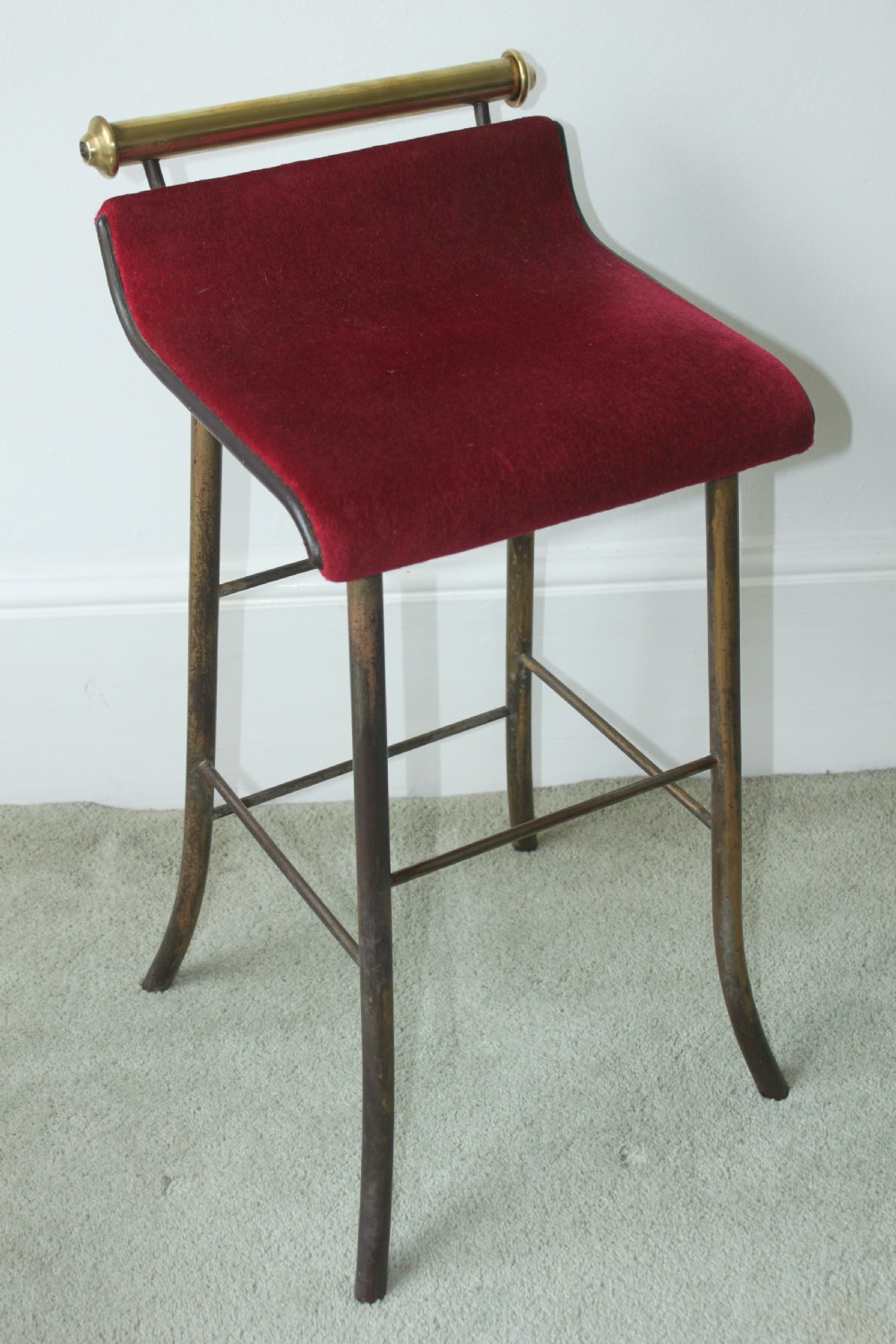 A 19th-century metal music stool featuring a red velvet seat, curved steel legs, and a cylindrical brass top rail with end finials.
