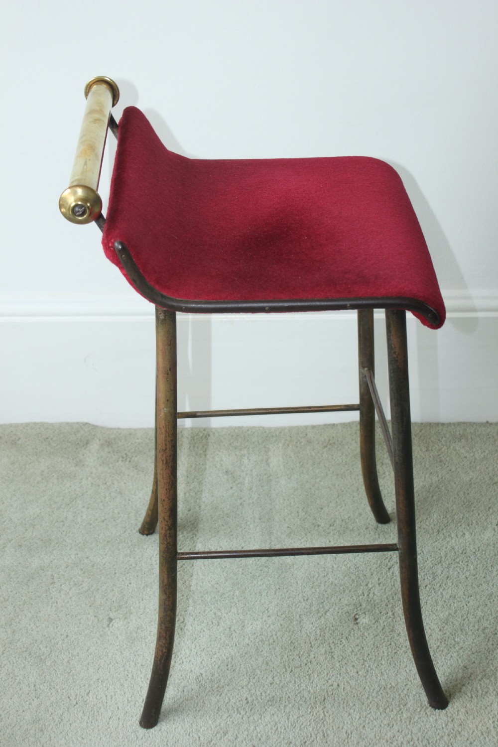 A 19th-century metal music stool featuring a red velvet seat, curved steel legs, and a cylindrical brass top rail with end finials. View II