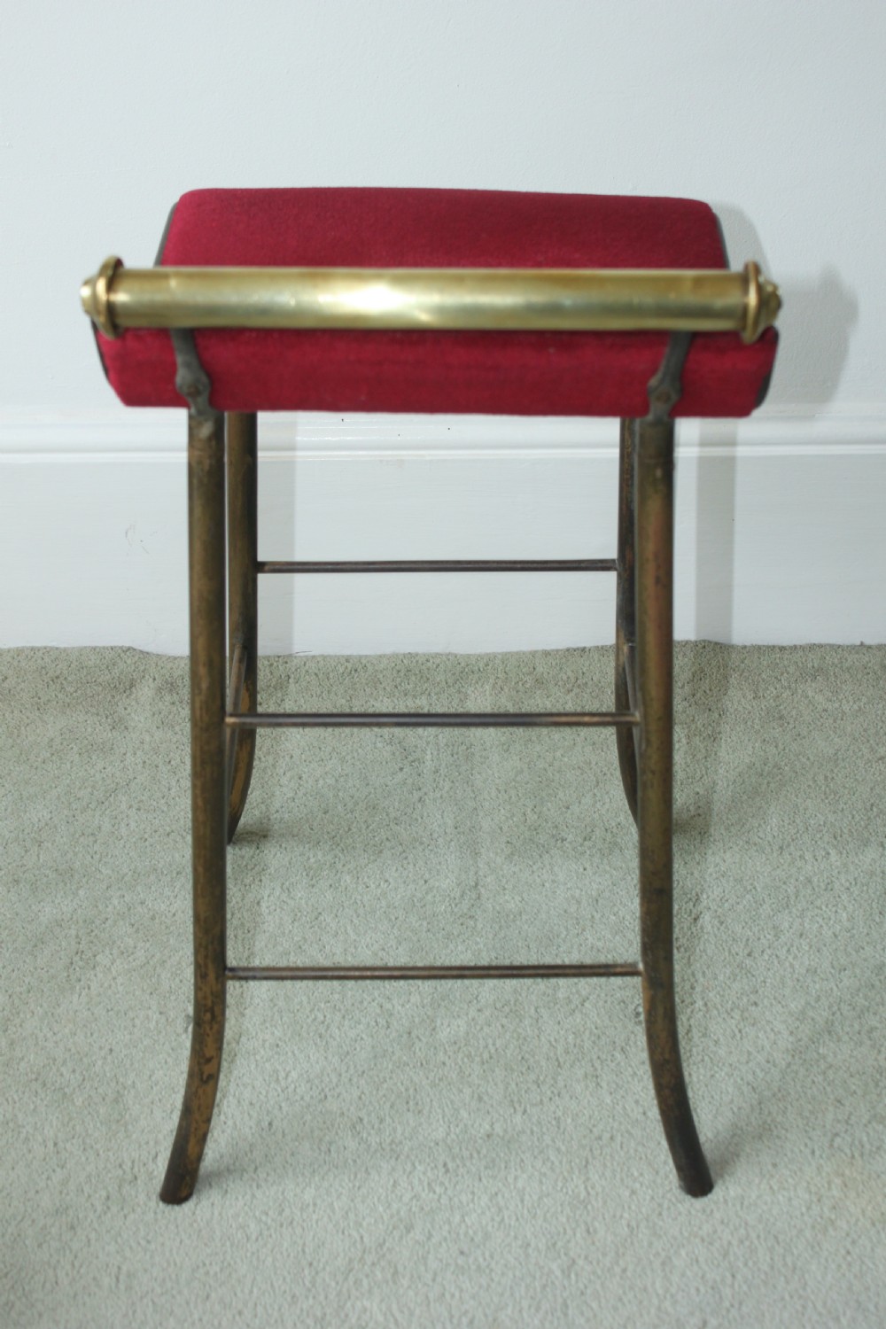 A 19th-century metal music stool featuring a red velvet seat, curved steel legs, and a cylindrical brass top rail with end finials. View III