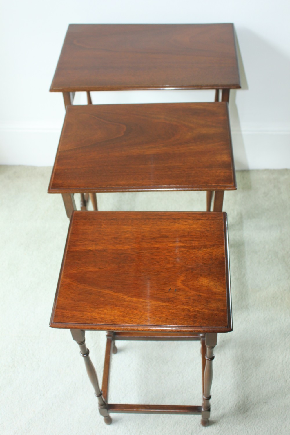 A set of three graduated mahogany Edwardian nesting tables with turned legs standing nested together. View V