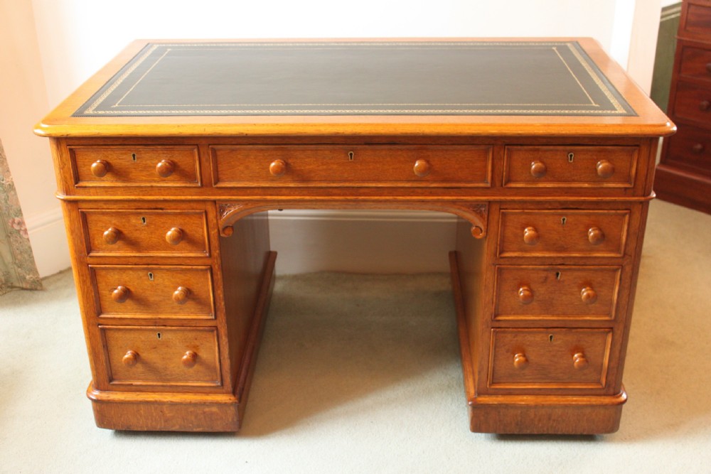 A 19th-century oak pedestal desk featuring a dark green leather writing surface with gold tool gilding, nine drawers with turned wooden knobs, and decorative carved kneehole spandrels. View II