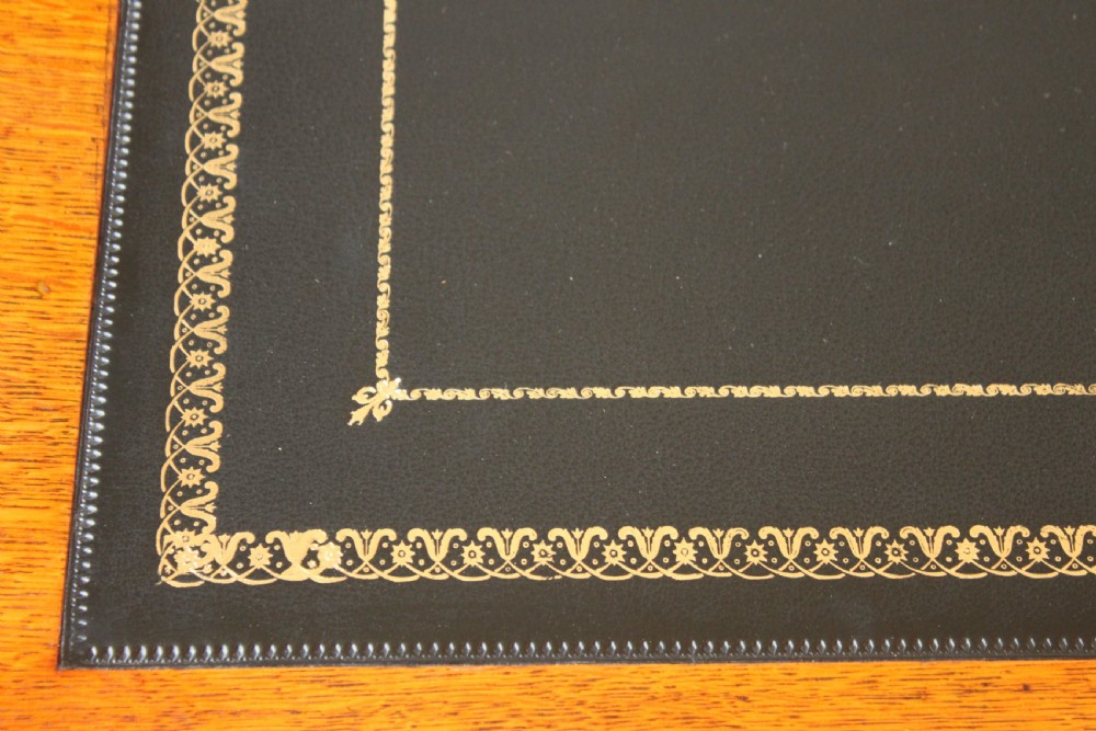 A 19th-century oak pedestal desk featuring a dark green leather writing surface with gold tool gilding, nine drawers with turned wooden knobs, and decorative carved kneehole spandrels. View VIII