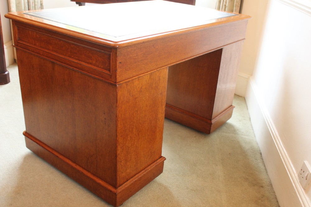 A 19th-century oak pedestal desk featuring a dark green leather writing surface with gold tool gilding, nine drawers with turned wooden knobs, and decorative carved kneehole spandrels. View IX
