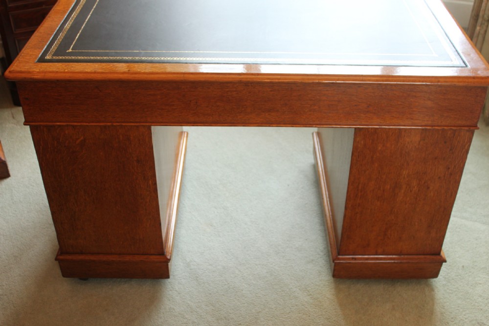 A 19th-century oak pedestal desk featuring a dark green leather writing surface with gold tool gilding, nine drawers with turned wooden knobs, and decorative carved kneehole spandrels. View X