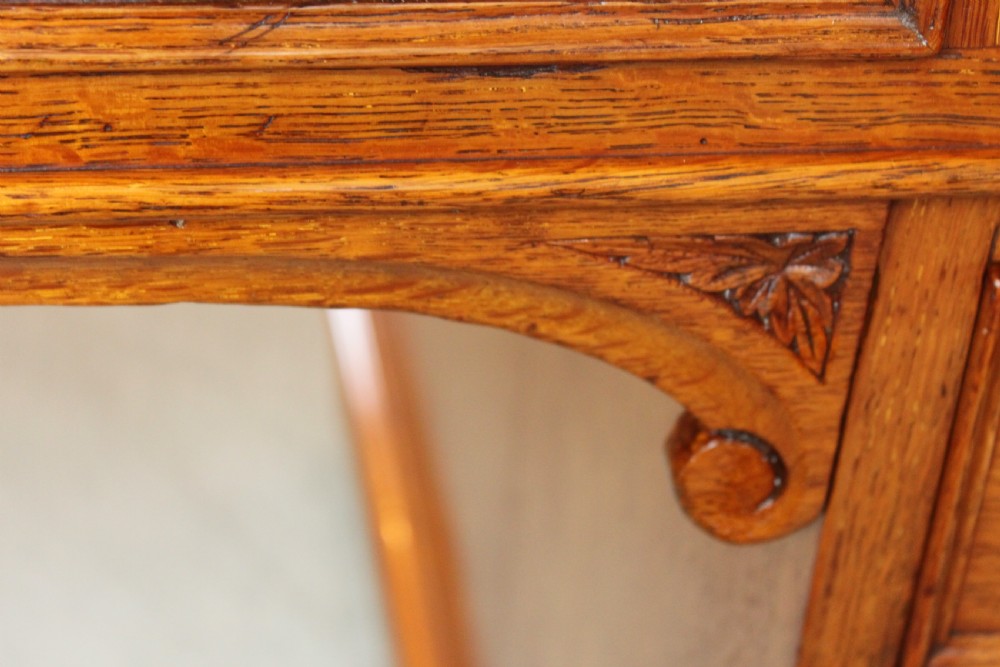 A 19th-century oak pedestal desk featuring a dark green leather writing surface with gold tool gilding, nine drawers with turned wooden knobs, and decorative carved kneehole spandrels. View XIII