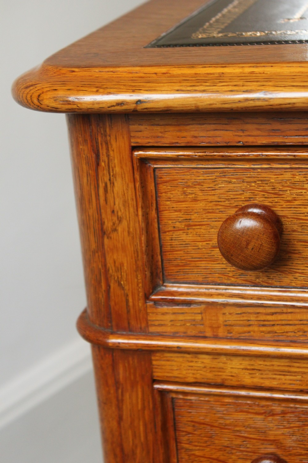 A 19th-century oak pedestal desk featuring a dark green leather writing surface with gold tool gilding, nine drawers with turned wooden knobs, and decorative carved kneehole spandrels. View XIV