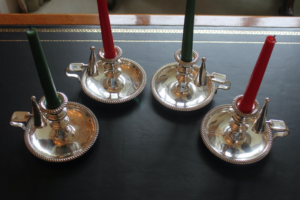 A set of four early nineteenth-century silver-plated chambersticks with circular drip pans, gadrooned rims, curved handles, and conical extinguishing snuffers.