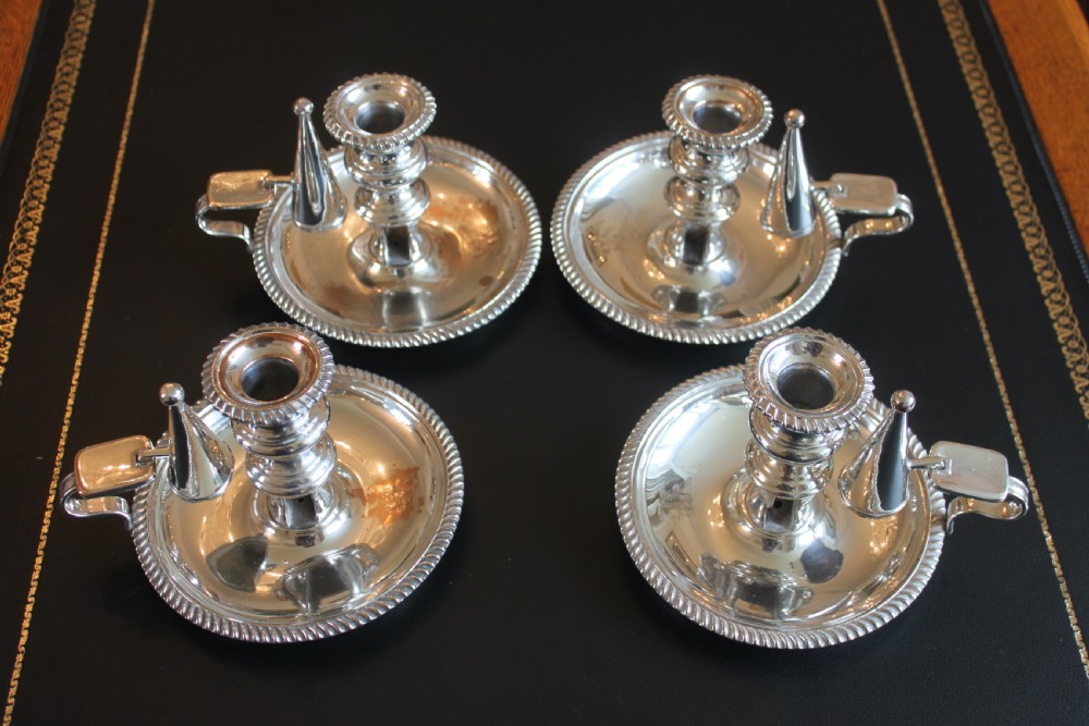 A set of four early nineteenth-century silver-plated chambersticks with circular drip pans, gadrooned rims, curved handles, and conical extinguishing snuffers. View V