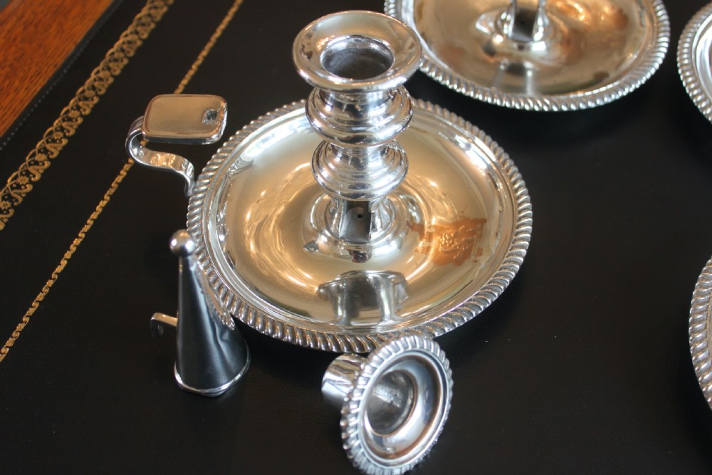 A set of four early nineteenth-century silver-plated chambersticks with circular drip pans, gadrooned rims, curved handles, and conical extinguishing snuffers. View X